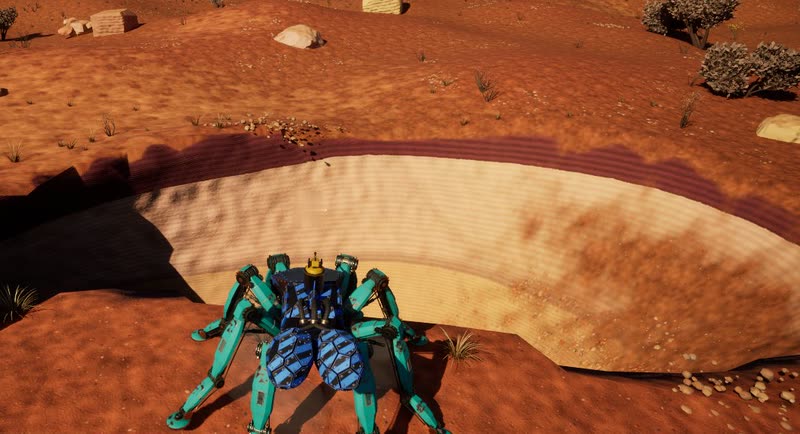 A teal spider mech with blue armour plates at the lip of a sandstone ledge, looking over the canyon floor.